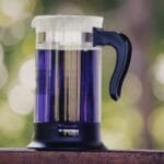 French press z fioletowym napojem na drewnianym stole na zewnątrz