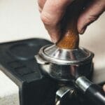 Barista ubija kawę w kolbie tamperem przed zaparzeniem espresso