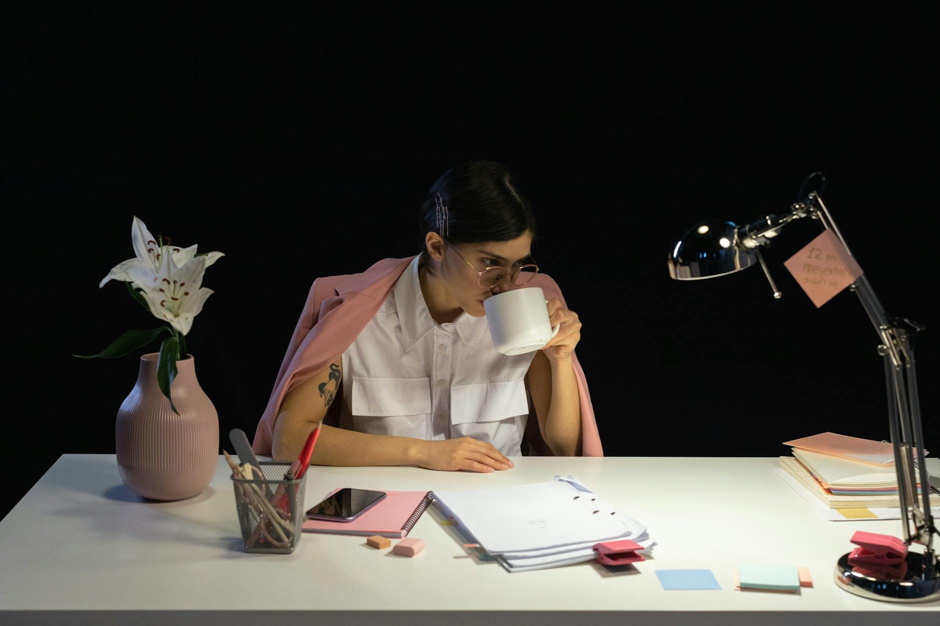 Młoda kobieta pijąca kawę przy biurku w biurze, obok kwiaty i laptop