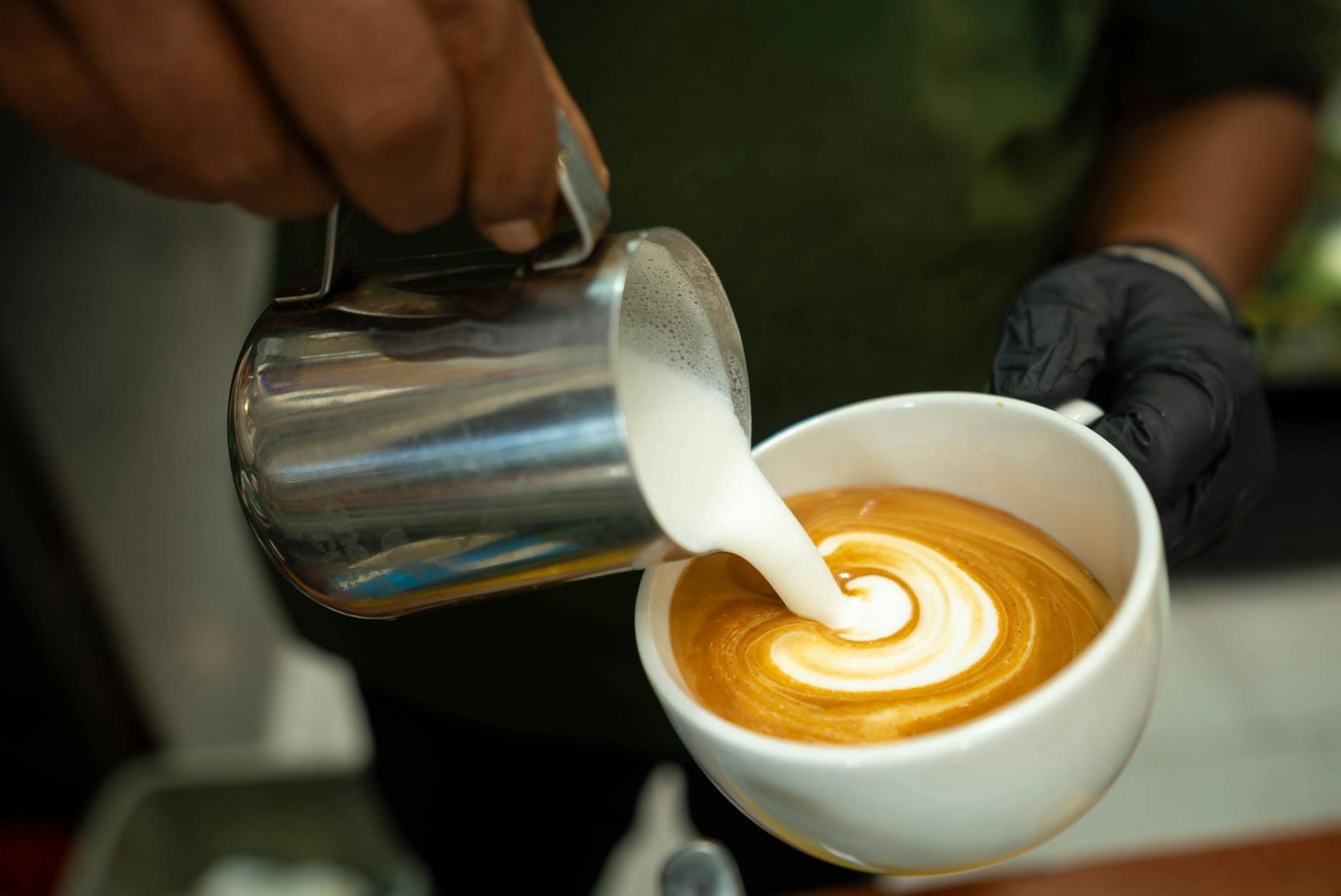 Barista wlewa spienione mleko, tworząc latte art na cappuccino