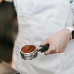 Barista trzyma kolbę z równomiernie zmieloną kawą przy ekspresie