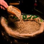 Dłoń wsypuje surowe ziarna kawy do jutowego worka