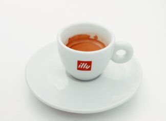 Kawa na czczo: czy picie espresso przed śniadaniem niszczy żołądek? Biała filiżanka espresso Illy ze spodkiem na jasnym tle