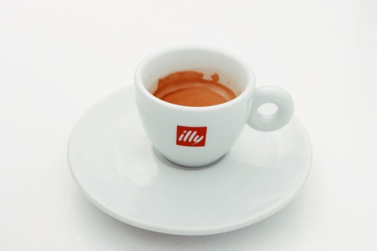 Biała filiżanka espresso Illy ze spodkiem na jasnym tle